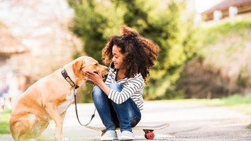 African american girl outdoors on skateboard with her dog.